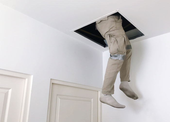 Person's legs hanging from ceiling hatch, creating weird and scary scene caught on security tape.