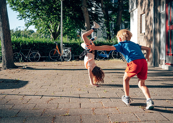 Two children playing outside, one doing a handstand while the other reaches out, captured in security tape footage.