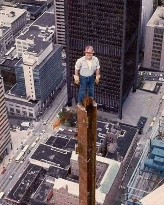 Man in a hard hat and gloves standing atop a tall steel beam high above a city, showcasing a weird history moment.