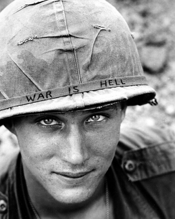 Young soldier wearing a helmet with war is hell written, representing weird things about history in black and white photo.