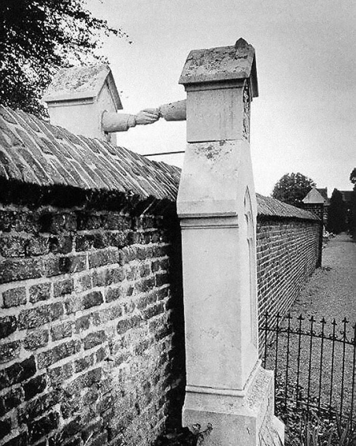 Black and white photo showing two chimney stacks with sculpted hands reaching out to shake over a brick wall, history weird facts.