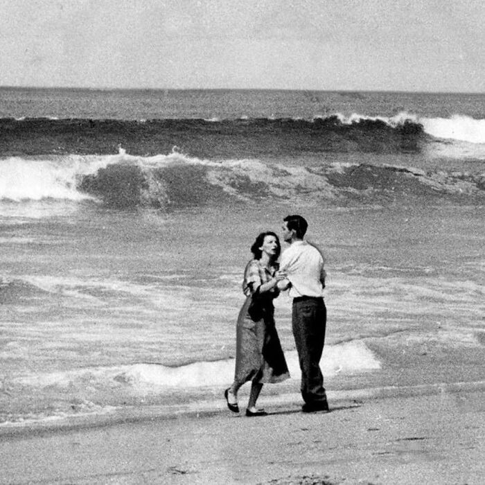 Black and white photo of a couple dancing on the beach with waves behind, illustrating weird things about history.