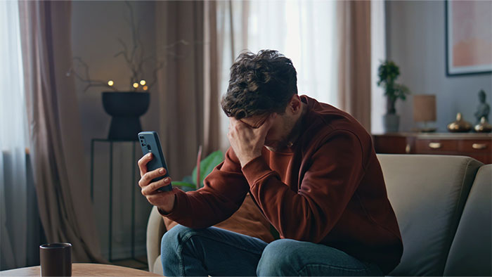 Man sitting on a couch holding a phone with his hand on his face, depicting frustration and relationship icks.