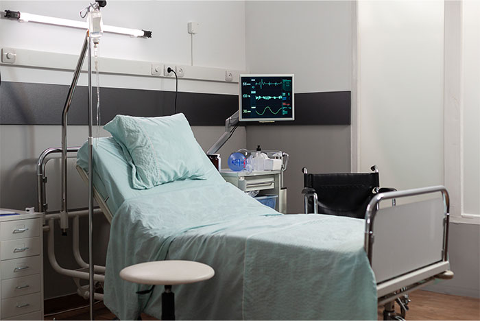 Hospital bed with medical equipment and a wheelchair in a clean, well-lit patient room setting.