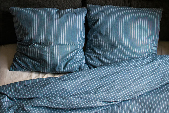 Blue striped pillows and bedding on an unmade bed, symbolizing relationship icks shared by women about men.