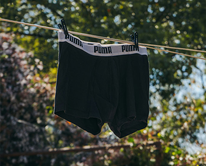 Black Puma boxer shorts hanging on a clothesline outdoors with trees and sunlight in the background.