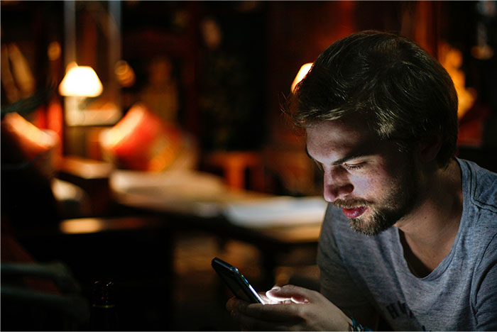 Young man in a dimly lit room looking at his phone, illustrating common icks women shared about men in relationships.