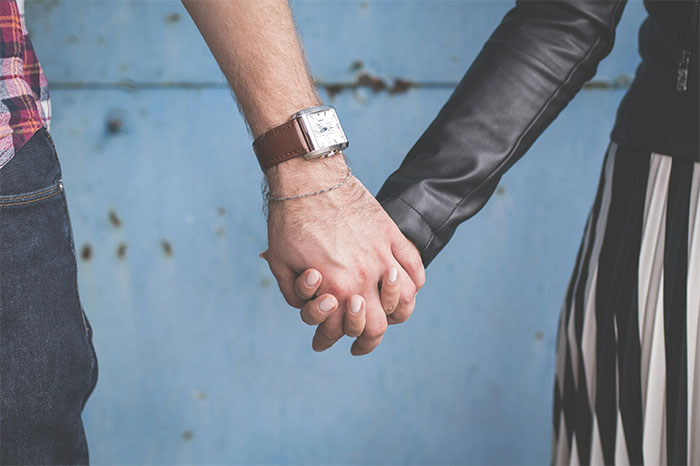 Couple holding hands with focus on their hands and casual clothing against a blue textured background.