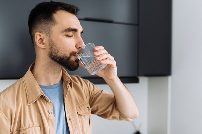 Young man with a beard drinking water indoors, representing typical icks women notice in men they dated.