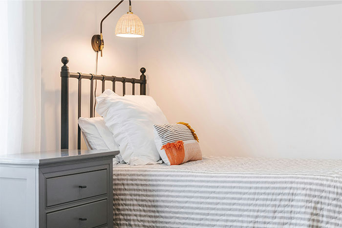 Minimalist bedroom with striped bedding and pillows, featuring cozy decor and soft lighting by a bedside lamp.