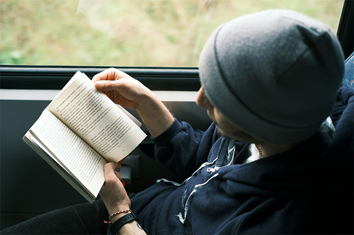Man wearing a gray beanie reading a book by the window, highlighting relationship icks women shared about men