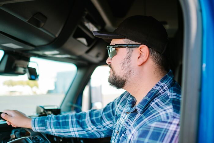 Truck driver wearing sunglasses and a cap, focused on driving a large vehicle, representing creepy and scary moments.