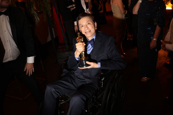 Actor James Hong in a wheelchair holding an award, representing actors who have been in the most movies across every genre.