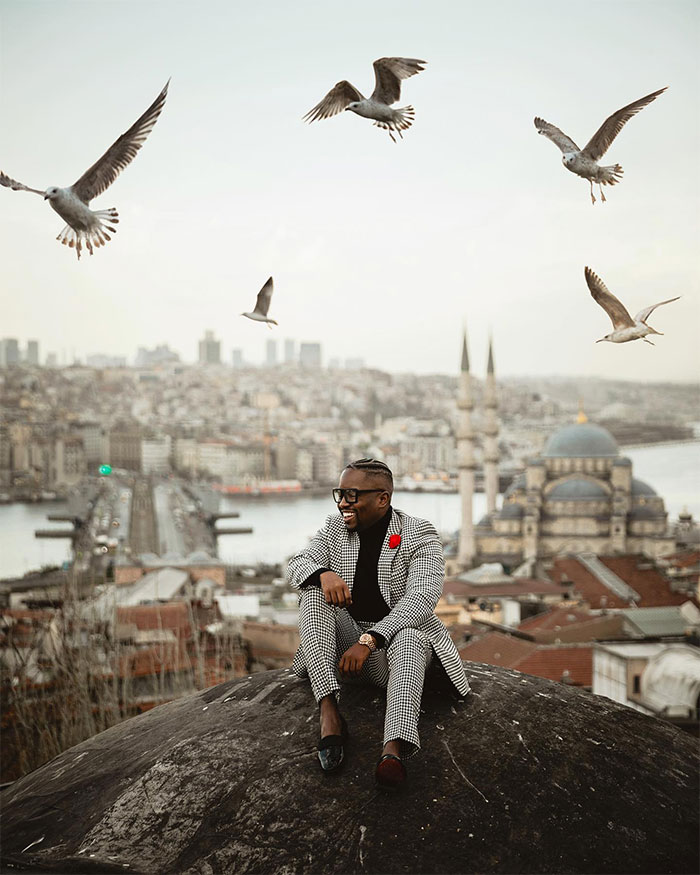 Man in stylish suit sitting outdoors with birds flying above, illustrating the public health risk of bird poops on you.