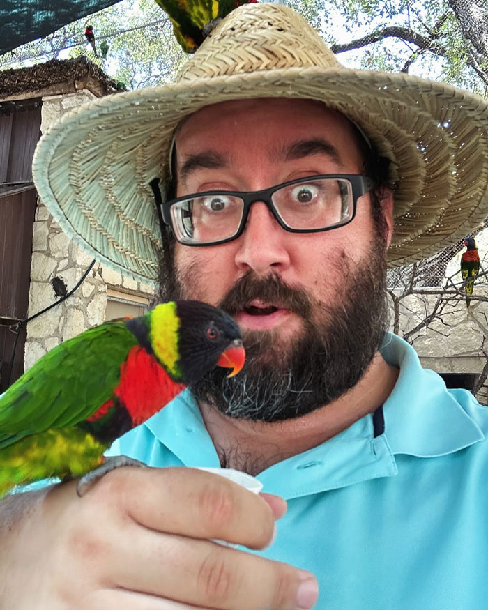 Man wearing glasses and a straw hat holding a colorful bird highlighting bird poop as a public health risk and omen.
