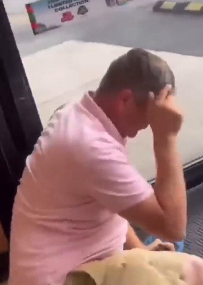 Man in pink shirt seated indoors after store brawl involving slur and confrontation with Black shopper.
