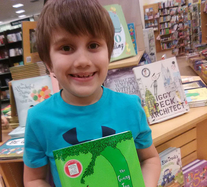 Young boy smiling in bookstore holding The Giving Tree book, related to 16 And Pregnant star Whitney Purvis news.