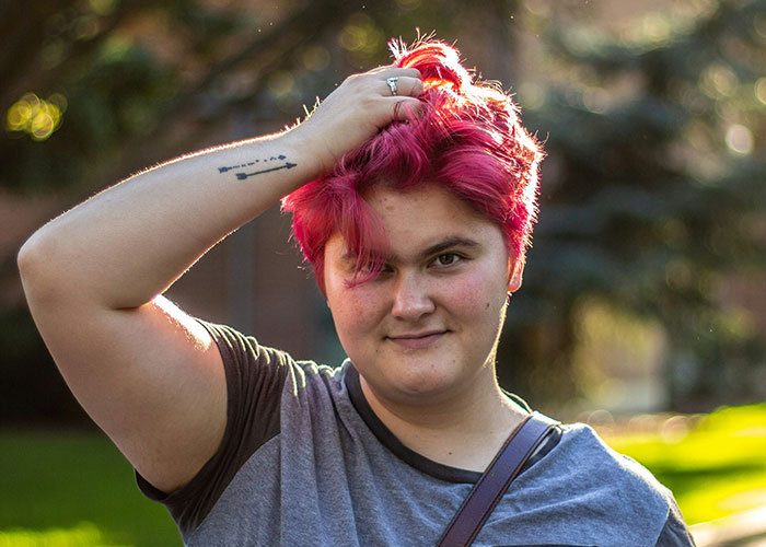 Person with bright red hair smiling outdoors, reflecting on wholesome interactions with strangers in a thoughtful setting.