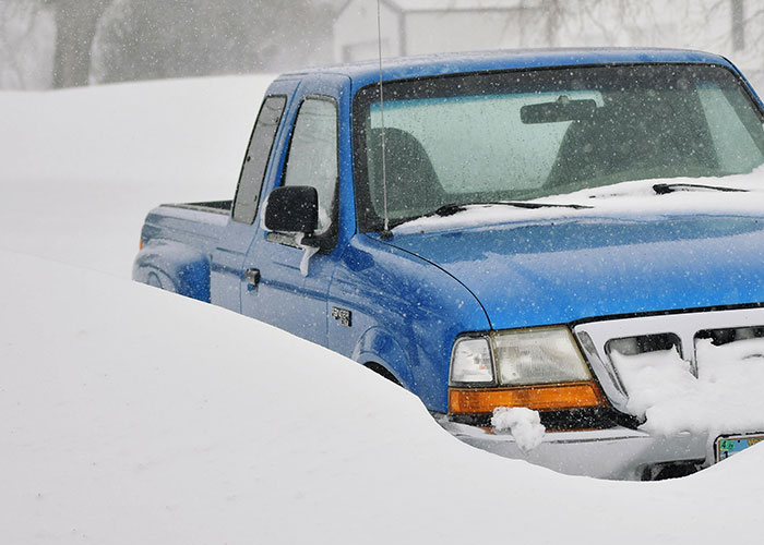 Blue pickup truck partially buried in snow during a heavy snowfall, evoking wholesome interactions with strangers in winter.