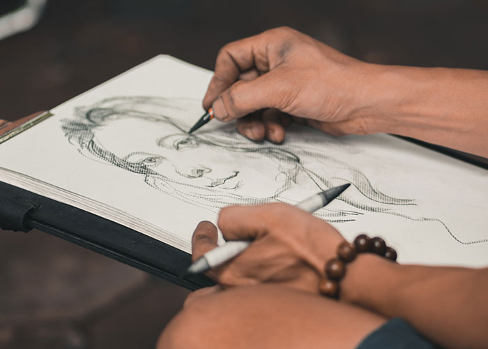 Artist sketching a portrait in a notebook, capturing a wholesome interaction during a creative moment with strangers.