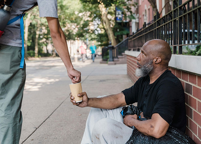 Person giving a cup to a homeless man, capturing a wholesome interaction between strangers on a city sidewalk.