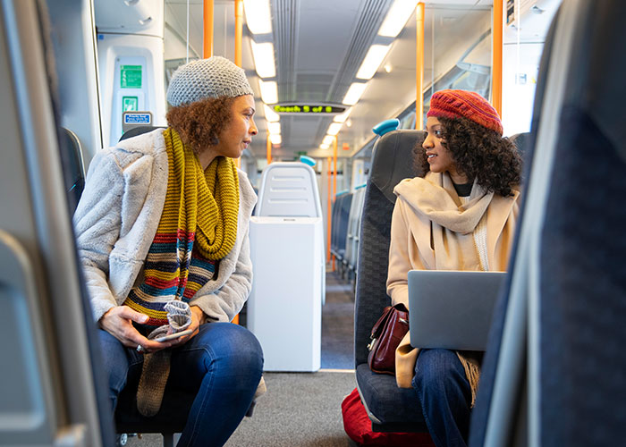 Two women sharing a wholesome interaction with a stranger on public transportation, smiling and engaged in conversation.
