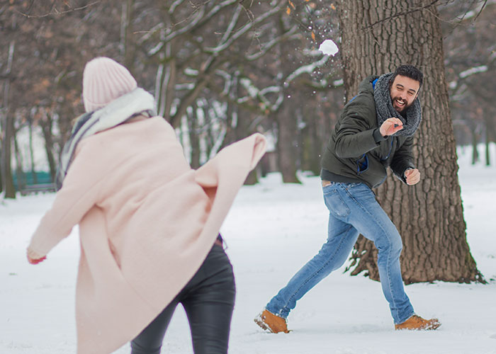 Two people enjoying a wholesome interaction with strangers, playfully throwing snow in a snowy park setting.