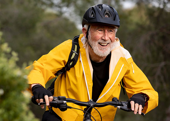 Smiling elderly man wearing a helmet and yellow jacket enjoying a bike ride, representing wholesome interactions with strangers.