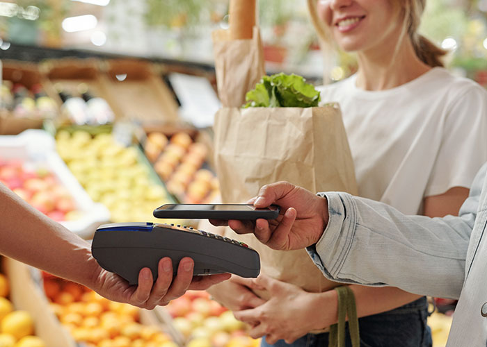 Customer making a contactless payment at grocery store, sharing a wholesome interaction with a stranger while shopping.