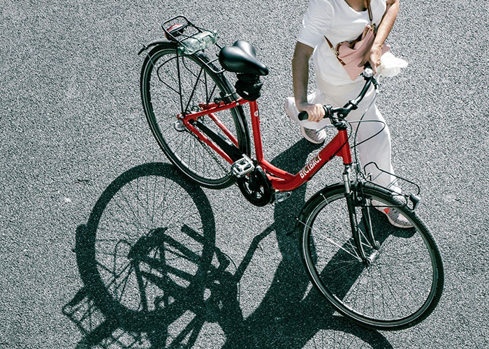 Person walking a red bicycle on a sunlit street, representing wholesome interactions with strangers and positive moments.