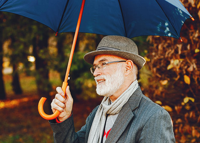 Elderly man smiling warmly while holding an umbrella, representing wholesome interactions with strangers outdoors.