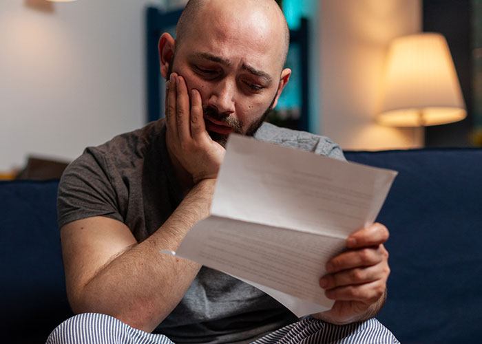 Man sitting on couch looking emotional while reading a letter, reflecting on wholesome interactions with strangers.