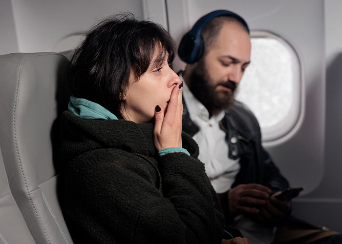 Woman appearing thoughtful seated next to a man on a plane, reflecting a wholesome interaction with a stranger moment.