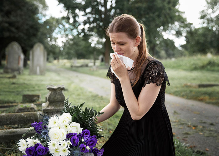 Woman wiping tears while holding flowers at a gravesite, reflecting on wholesome interactions with strangers.