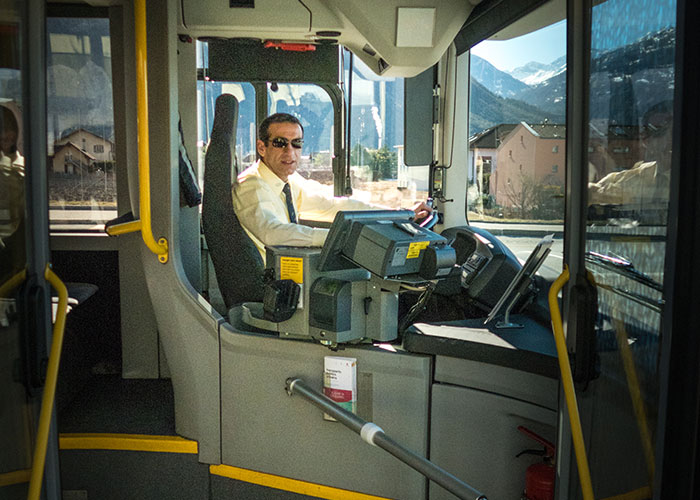 Bus driver in sunglasses smiling at the camera, capturing a wholesome interaction with strangers on a bright day.