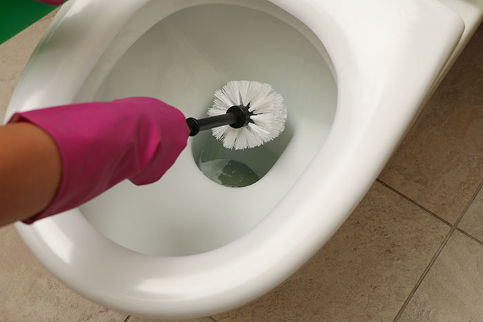 Hand in pink glove holding toilet brush inside toilet bowl showing product design flaws causing frustration.