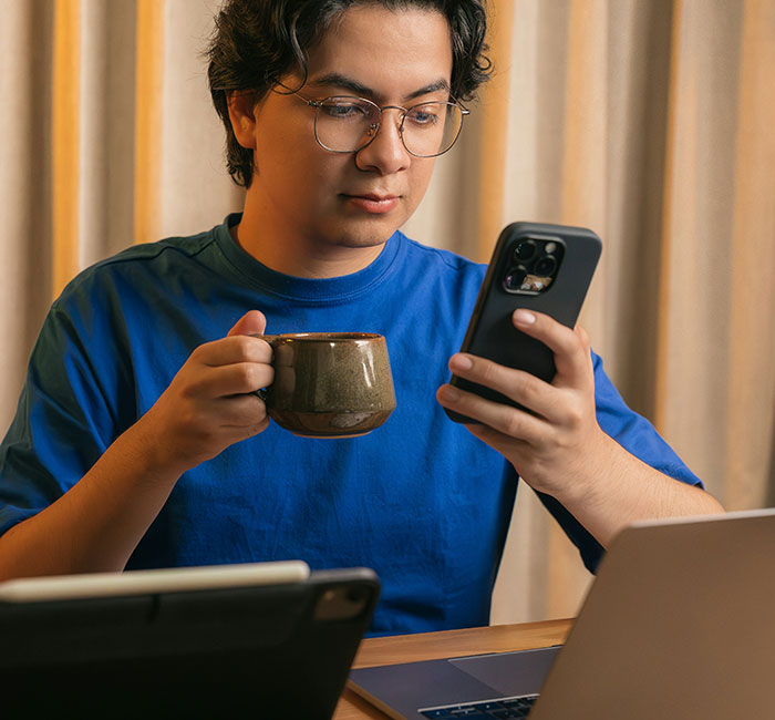 Person in blue shirt holding a cup and smartphone, surrounded by devices, illustrating products with design flaws frustration.