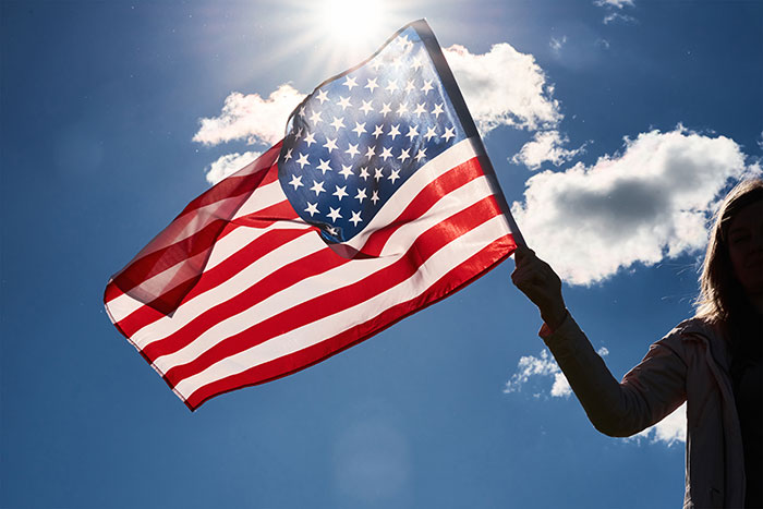Person holding an American flag waving against a sunny sky, illustrating design flaws causing frustration with products.