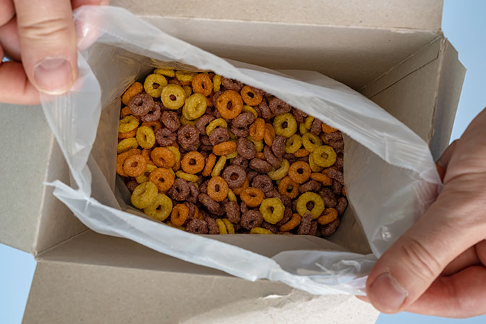 Hands opening a cereal box showing product design flaws with a poorly filled bag frustrating users every time.