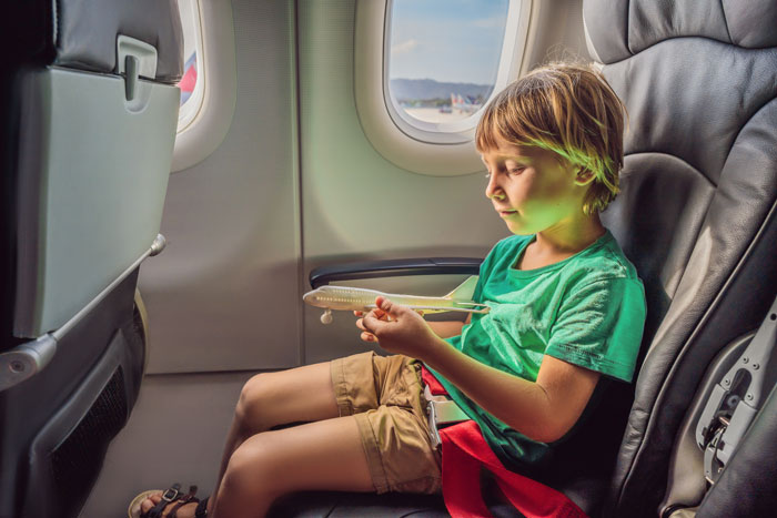 Child playing with toy airplane while seated on 10-hour flight, illustrating mom insists woman give up her seat conflict.