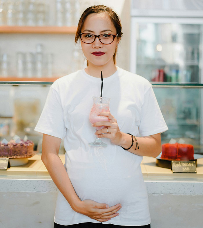 Pregnant woman holding a drink and gently touching her belly in a cafe, offering advice to an upset coworker.