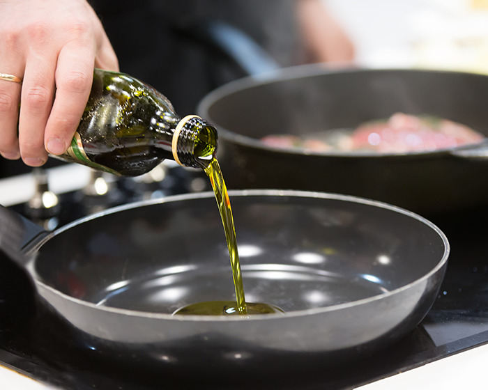 Woman pouring olive oil into a frying pan preparing for a unique egg frying technique in a kitchen setting. Woman pouring olive oil into a frying pan preparing for a unique egg frying technique in a kitchen setting.