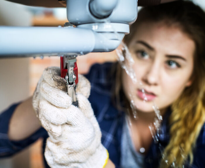 Woman using a wrench to fix a leaking pipe, demonstrating uncommon hacks for women living alone in home maintenance.