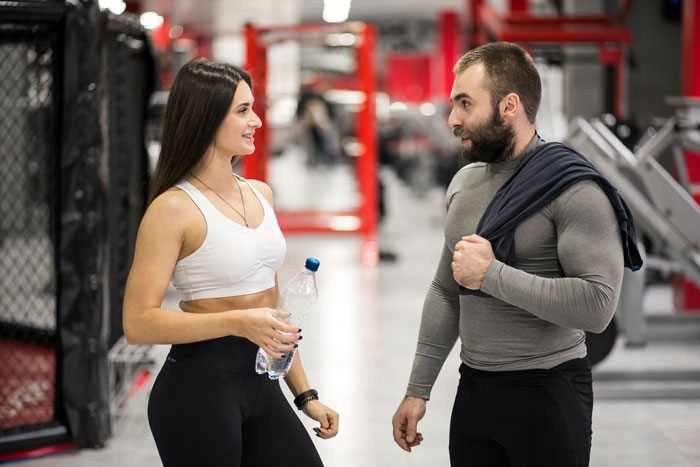 Man and woman in gym setting, man avoiding gym stalker as she flirts while holding a water bottle.