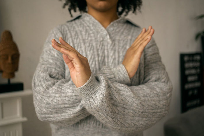 Woman listed as emergency contact crossing arms in refusal gesture, wearing gray sweater in indoor setting.