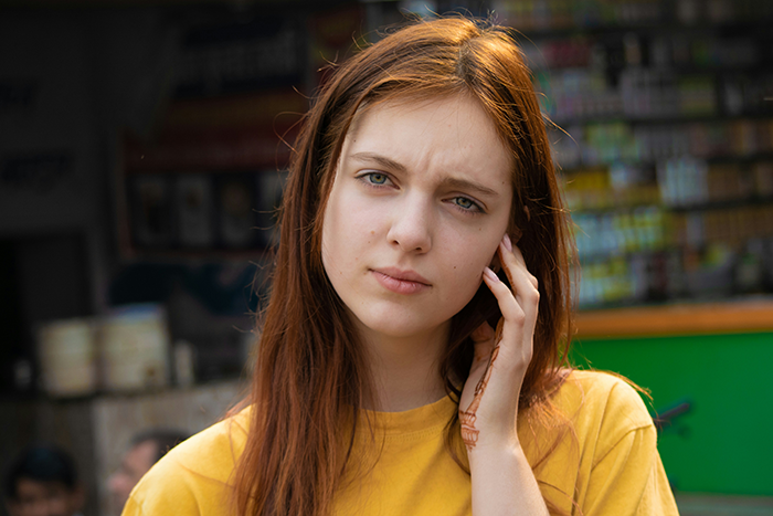 Young woman in a yellow shirt looking thoughtful, representing a woman move Alaska alone decision moment outdoors.