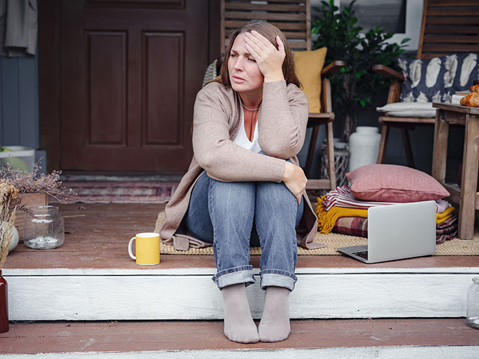 Woman sitting on porch steps looking stressed after roommates and sisters find out she secretly owns the house