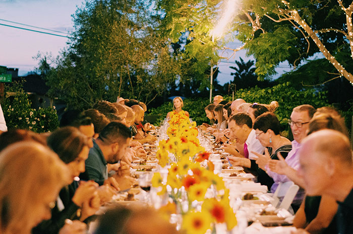 Large group dining outdoors at a wedding dinner with kosher meals, featuring bright yellow floral centerpieces on the table.