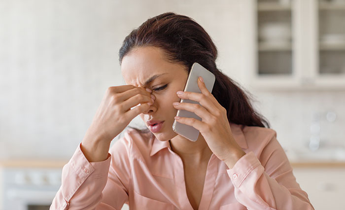 Stressed woman on phone in kitchen, depicting tension related to babysitter refuses to watch one specific child.