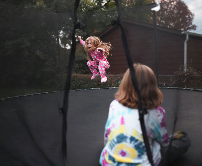 Young woman watching a child jump on a trampoline outdoors, highlighting family conflict over a broken leg claim.